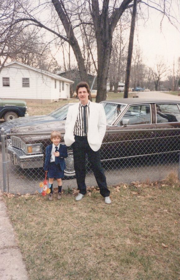 Mike in a white jacket standing with young Shane in front of the house