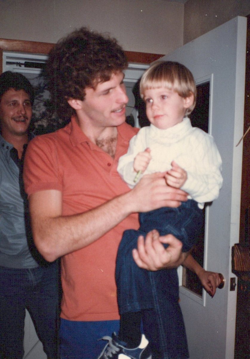 Mike in an orange shirt holding a smiling toddler Shane